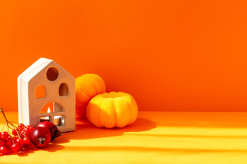 Halloween. Pumpkins, house, rowan tree and small apples on orange background
