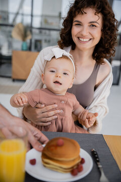 Man Serving Pancakes To Cheerful Wife With Infant Daughter During Breakfast.