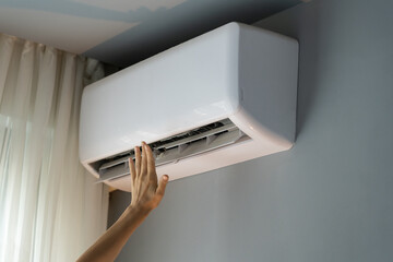 Female owner of apartment stretches hand to check operating air conditioner and catch stream of...