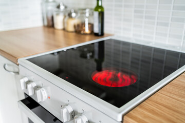 Stove and cooker red hot. Induction, ceramic cooktop, electric stovetop and hob in kitchen. Warm plate ready for cooking. Contemporary interior design, modern counter and wood table. - obrazy, fototapety, plakaty