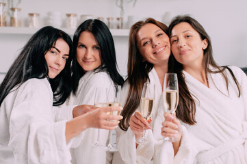 A group of women spend leisure time. Young attractive females in bathrobes drink champagne and chat merrily at home.
