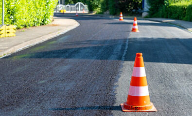 Construction cones marking part of road with a layer of fresh asphalt..
