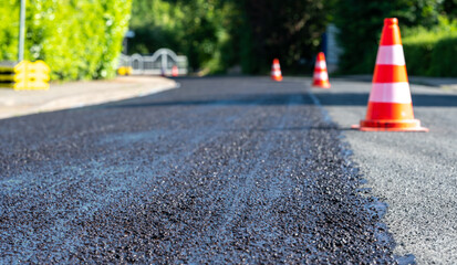 Construction cones marking part of road with a layer of fresh asphalt..