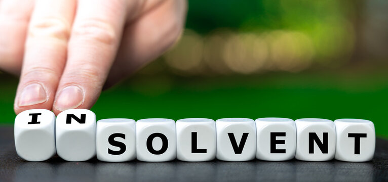 Hand turns dice and changes the word solvent to insolvent.