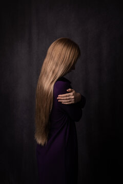 abstract studio portrait of side view of a blonde woman embracing herself in dark painterly style