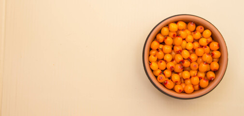 Fresh ripe of sea buckthorn berries in brown bowl. Top view. Beige background.