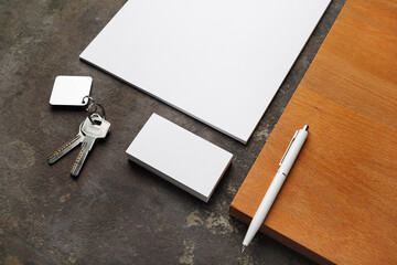 Blank stationery set and keys on concrete background.