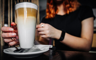 Female hands hold a glass of latte coffee in cafe