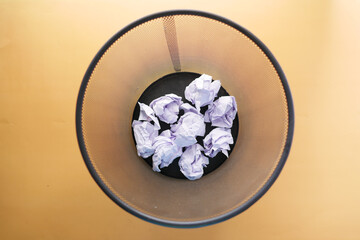 crumpled paper ball in a bin on orange color background top view 