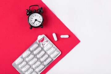 Capsule pills in blister pack and alarm clock on red and white. Sleeping pill with melatonin and taking medicine by schedule concept. Medical and pharmaceutical flat lay. Mockup copy space