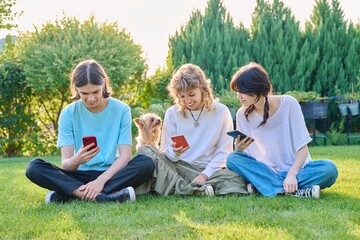 Naklejka premium Teenage friends sitting on the grass with smartphones