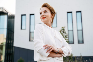 Portrait of confident middle aged businesswoman with arms crossed looking away outdoors  
