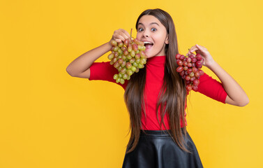 surprised girl hold bunch of grapes on yellow background