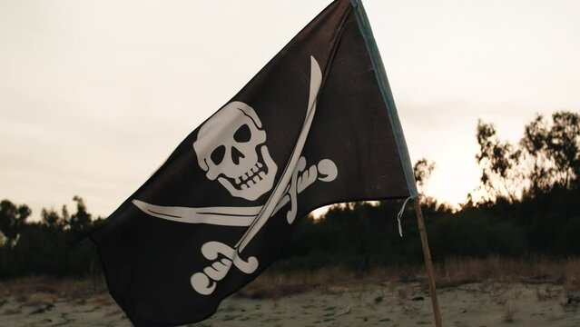Black pirate flag with skull symbol on the desert island