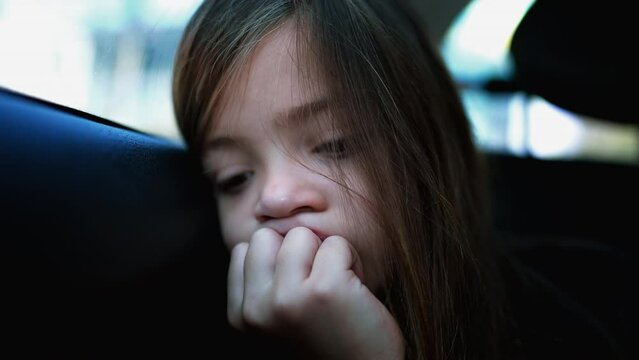 Sad little girl closeup face traveling by car leaning on car window backseat. Portrait of a bored sleepy child feeling bore and sadness