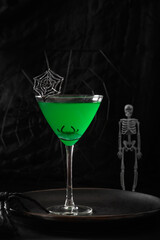 Halloween green cocktail decorated cobweb on black background. Horror funny food. Vertical format.