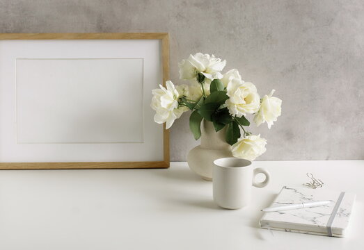 Modern home office workspace with photo frame mockup.  Aesthetic scandy hygge style.Cup coffee, photo frame,planner, vase with roses,pen .Copy space.Neutral colors home design.
