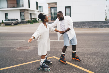 Cheerful ethnic man teaching girlfriend to riding roller skates