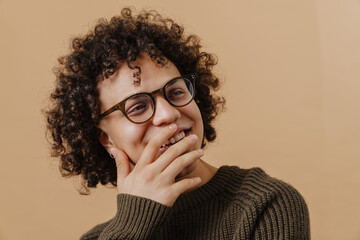 Young handsome curly smiling boy in glasses covering his mouth