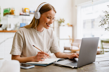 Young beautiful long-haired smiling woman in headphones doing her homework