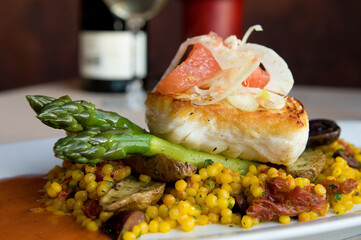 Seared halibut fillet on asparagus served with saffron-infused couscous, fingerling potatoes and...