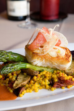 Seared halibut fillet with asparagus, saffron-infused couscous, fingerling potatoes and sun dried tomatoes in sauce. Grapefruit and shaved bulb fennel on top. Vertical Photo. 