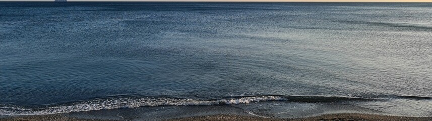 Genova, Italy- July 27, 2022:Panorama of the blue sea, light above the water, ocean sunrise. Some little waves in winter days. Clear sky reflected on the water.