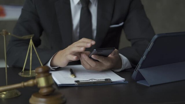 Online Lawyer Concept: Lawyer responds to smartphone messages with tablet and gold hammer and scales next to it.