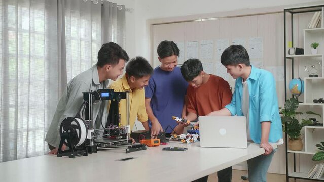 Group Of Young Asian Boys With A Laptop And 3D Printing Helping Each Other Assembling A Cyborg Hand While Working At Home
