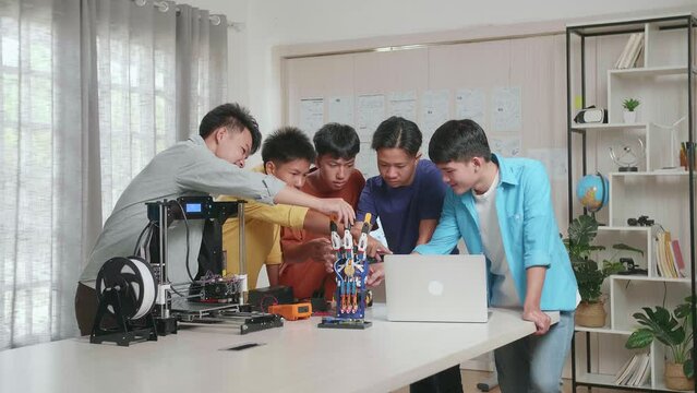 Group Of Young Asian Boys With A Laptop And 3D Printing Smiling To The Camera While Discussing About A Cyborg Hand At Home
