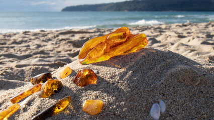 Transparent orange Baltic amber stone on a sand against the sea.  Ancient fossil.  Material for...