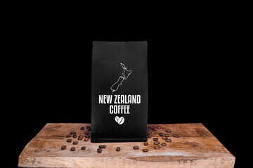 New Zealand coffee beans and black package on wooden board with black isolated background