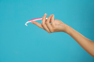 A female hand holds a disposable pink razor on a blue background