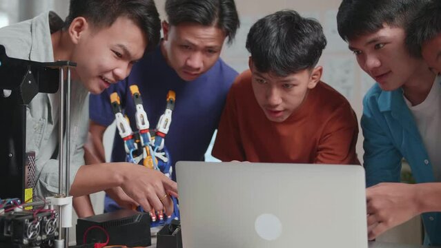 Group Of Young Asian Boys With 3D Printing Comparing A Cyborg Hand To The Pictures On A Laptop While Working At Home
