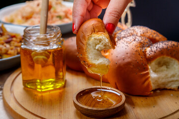 A woman's hand dips a piece of challah in honey in honor of the celebration of Rosh Hashanah nearby...