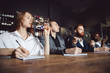 Sommeliers female and male tasting white wine and making notes at degustation card notepad