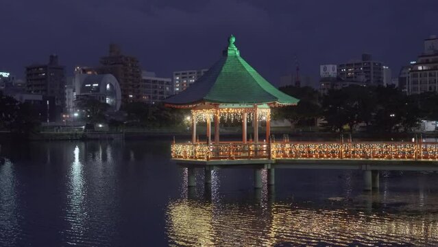 fukuoka, kyushu - december 06 2021: Pan video of the illuminated Ukimi-do Pavilion at night on the outer moat of Fukuoka Castle renamed Ohori Park depicting West Lake of China in Zhejiang Province.