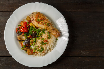 Rice with vegetables in sauce and chicken leg in a white plate on a wooden table.copy space