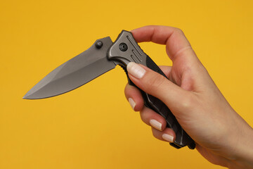 Folding knife in a female hand on an orange background. Close-up