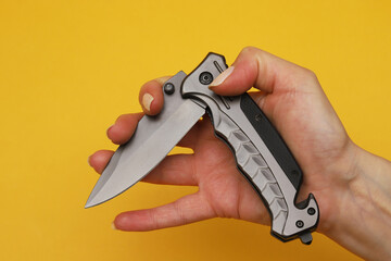 Folding knife in a female hand on an orange background. Close-up