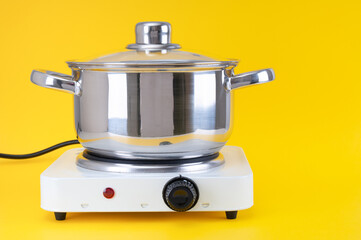 Stainless saucepan on portable electric stove close up on yellow background