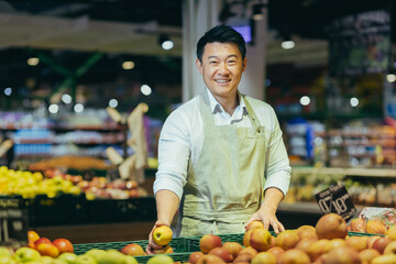 Portrait of Asian supermarket salesman, man in grocery vegetable section smiling and looking at camera.