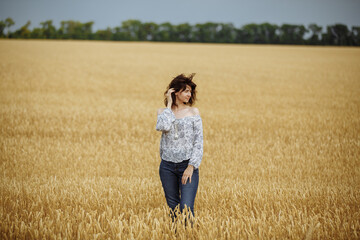 Naklejka na ściany i meble A girl in a field of yellow wheat on the background of a rainy sky