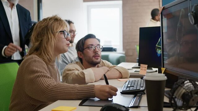 European woman, Caucasian male artist and CEO of company discuss the 3D model in a computer game and application development studio among other team members.