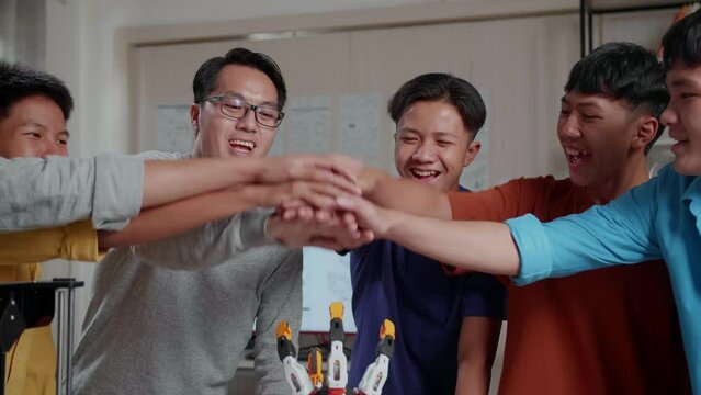 Asian Man And The Boys With A Laptop And 3D Printing Put The Hands Together And Scream Goal While Working About A Cyborg Hand At School
