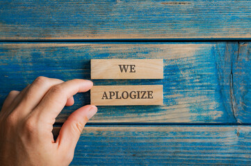 Male hand assembling a We apologize sign written on two wooden pegs - obrazy, fototapety, plakaty