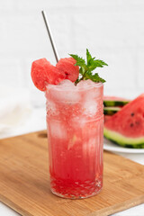 Watermelon smoothie or iced juice with watermelon slices and mint leaf on a white wooden background