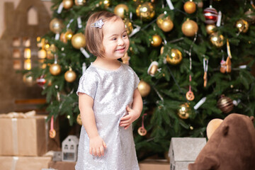 happy child girl with down syndrome smiles near the Christmas tree, enjoys christmas and presents on christmas eve