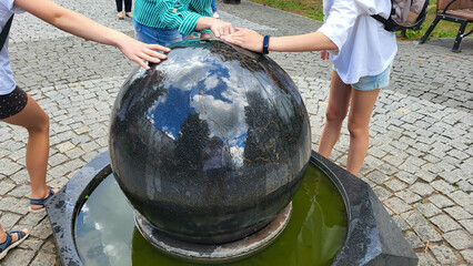 Black granite decorative fountain in the shape of a ball . Hands reach for the fountain