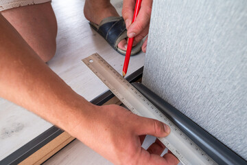 Installing a plinth in the room, measuring the required length using a square and a ruler, a gray...